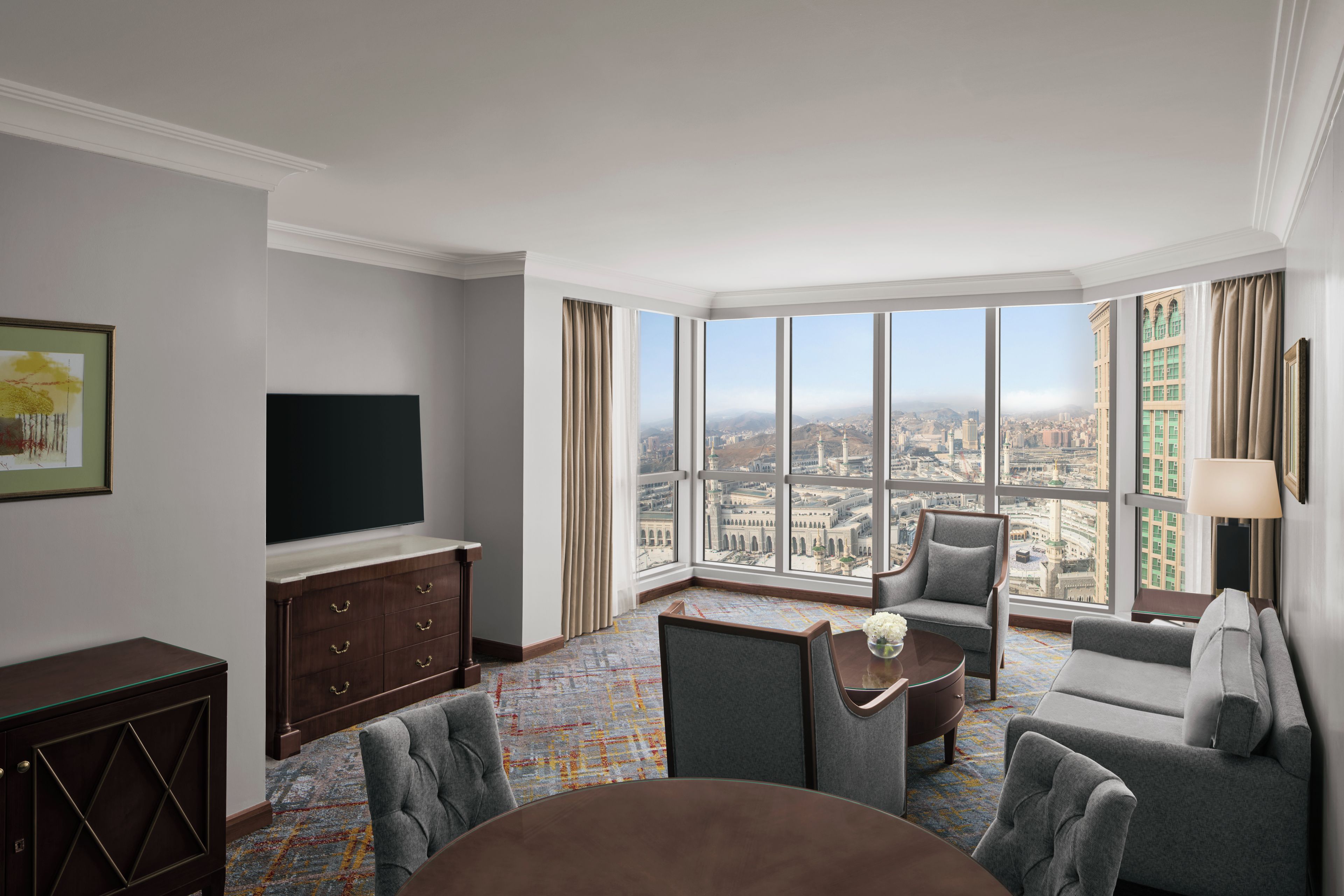 Hotelkamer met een groot raam met uitzicht op de stad, een flatscreen televisie, een bank, een stoel en een kleine tafel.