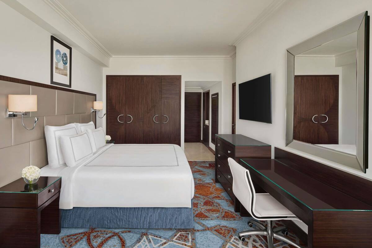 Een hotelkamer met een bed, nachtkastjes, een bureau met stoel, een grote spiegel en een kledingkast.