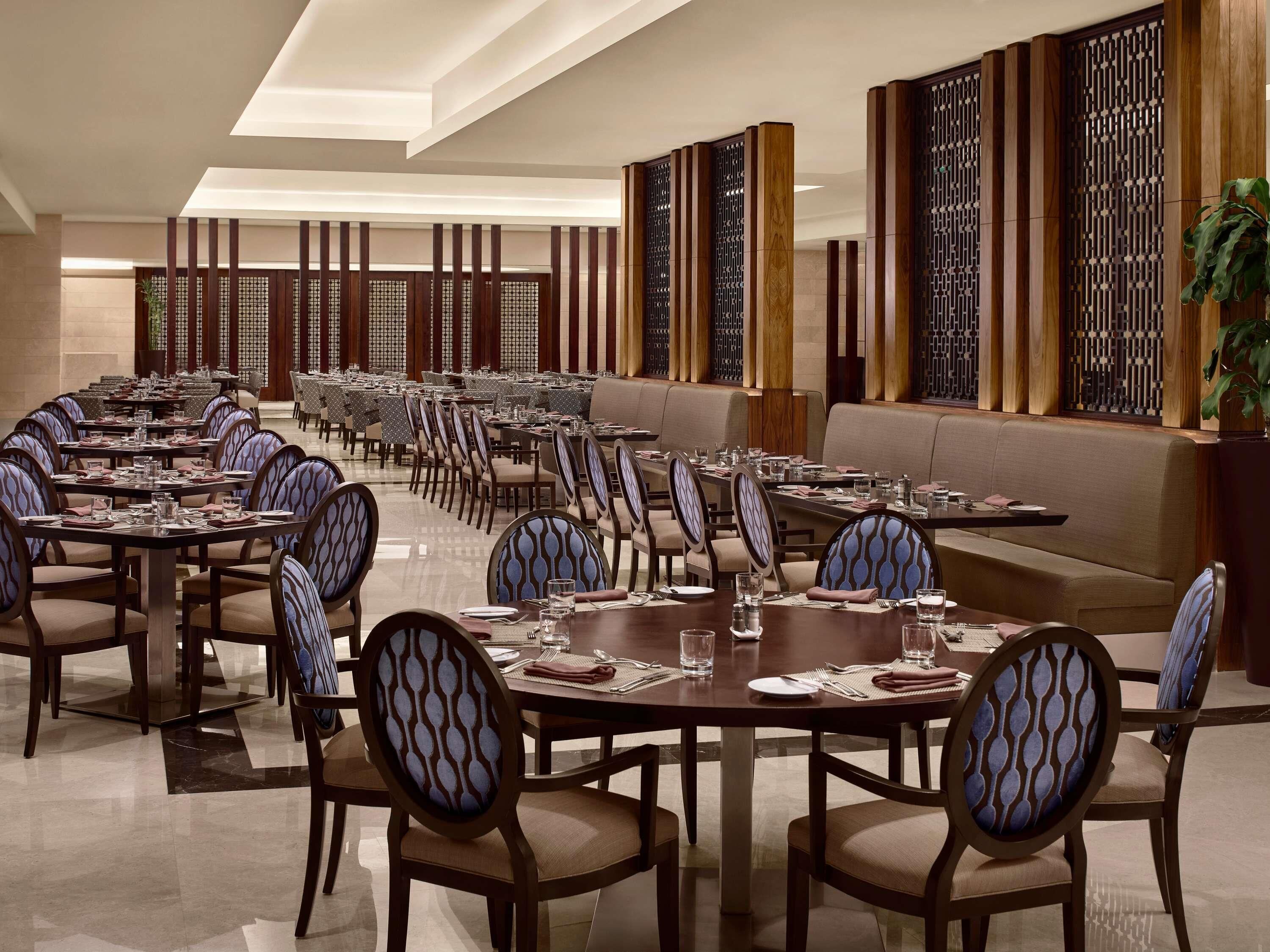 A spacious dining area with multiple tables and chairs, featuring a modern design with wooden accents and a patterned ceiling.