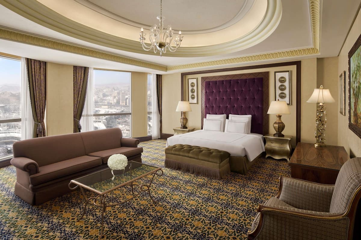 Hotelkamer met een groot bed, een sofa, een bijzettafeltje, een stoel, een kroonluchter en uitzicht over de stad.