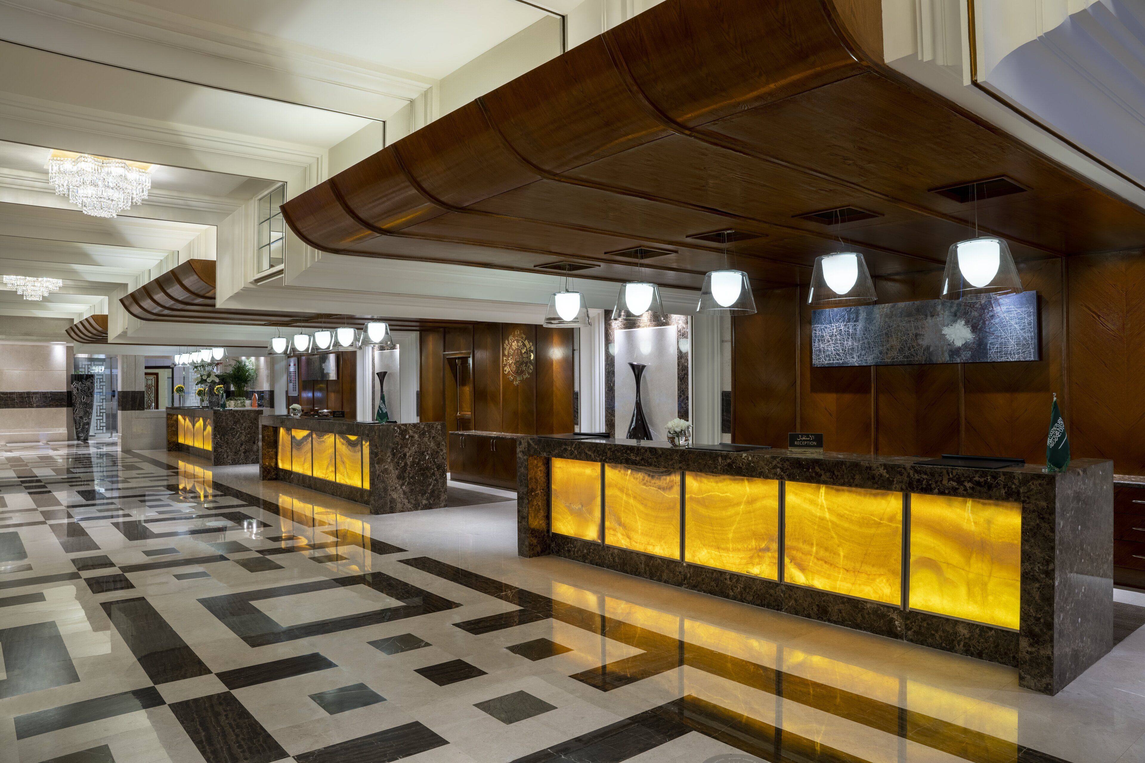 A hotel lobby with a check-in counter, a chandelier, and a patterned floor.