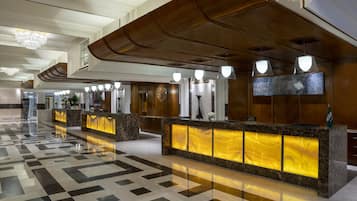 A hotel lobby with a check-in counter, a chandelier, and a patterned floor.