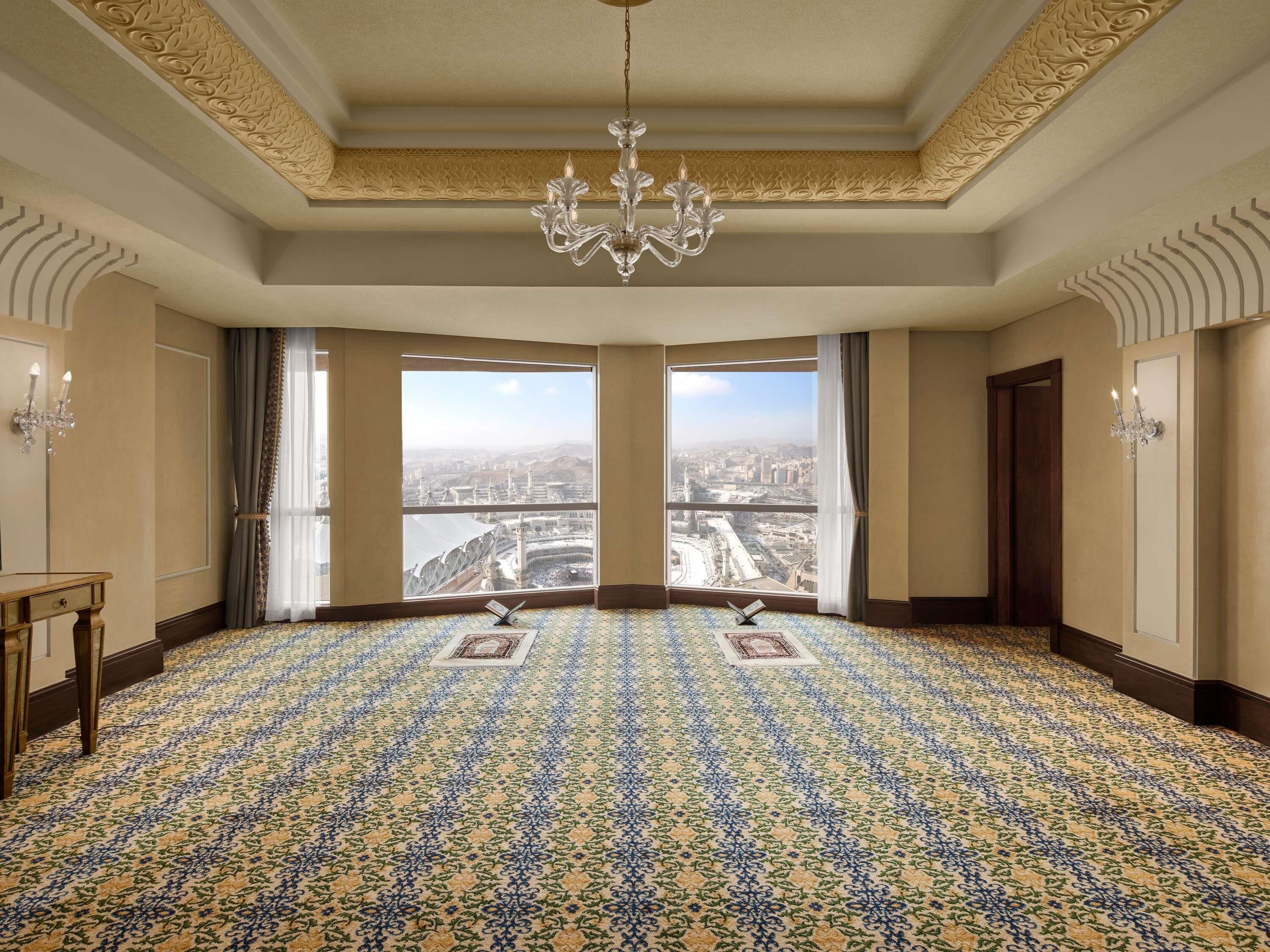 A room with a patterned carpet, a chandelier, and large windows offering a city view.