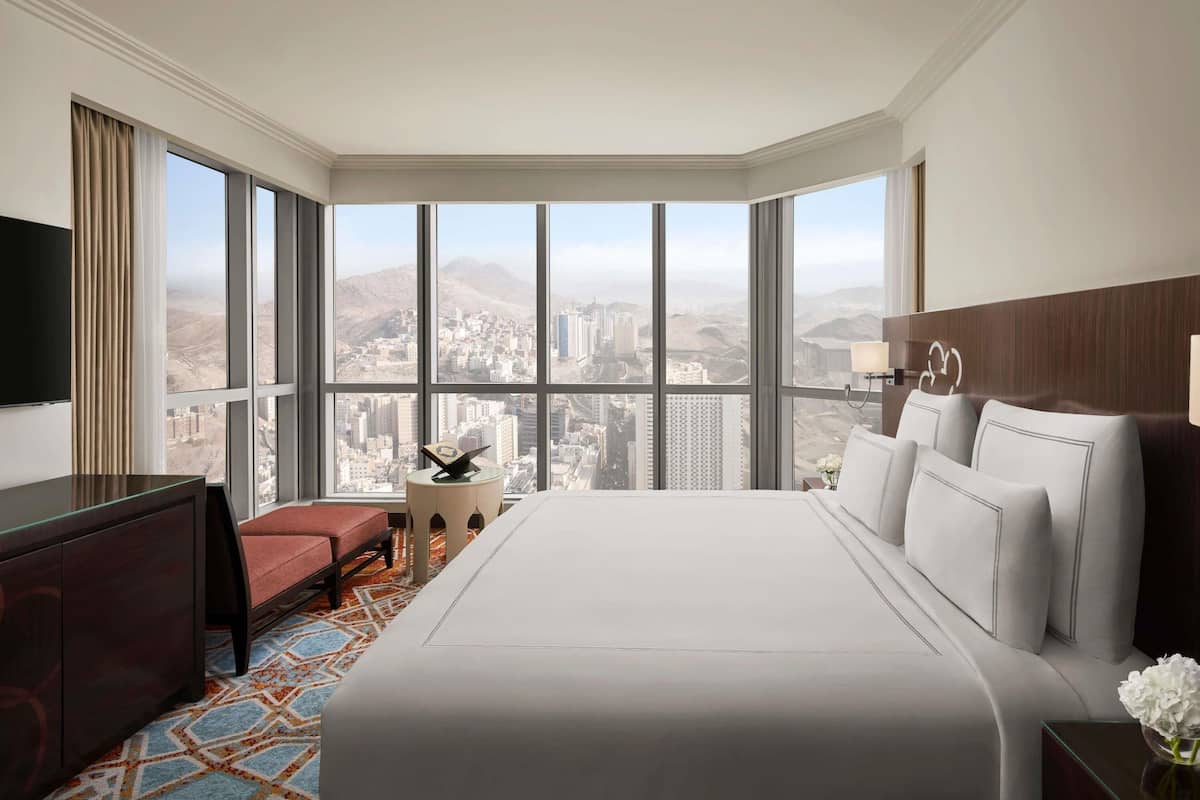 Een hotelkamer met een groot bed, een bureau, een stoel, een televisie en uitzicht op een stadsbeeld.