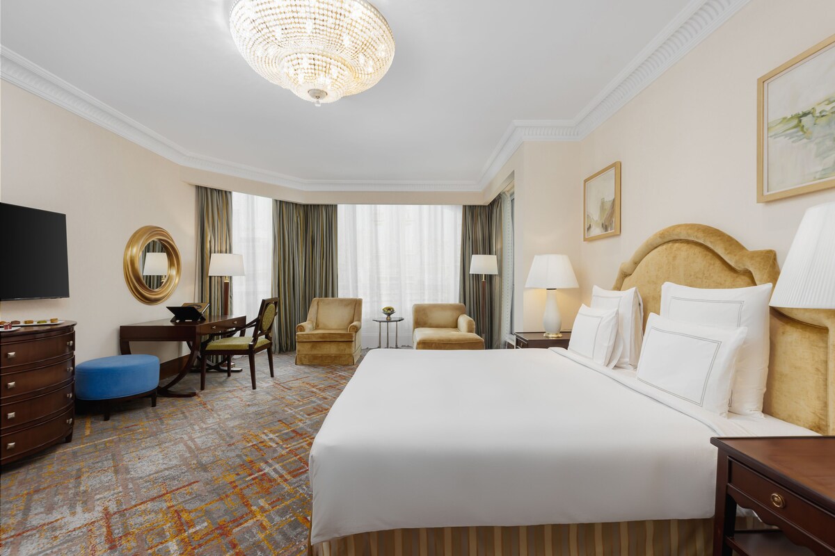 Ein Hotelzimmer mit einem großen Bett, einem Schreibtisch, zwei Stühlen, einem Fernseher und einer Chandelier.