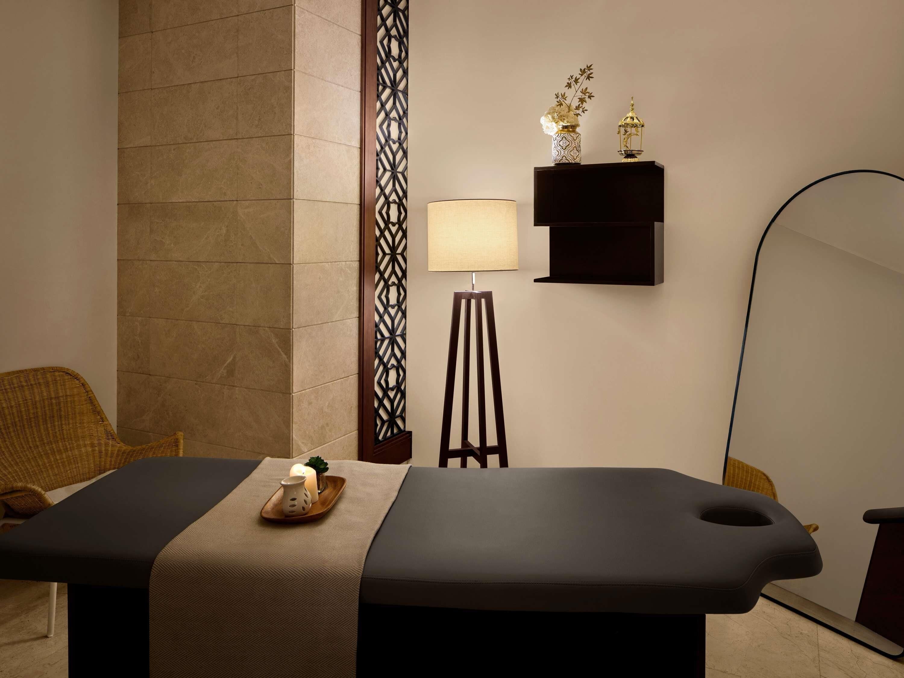 Une table de massage avec une serviette, une lampe, une étagère décorative et une chaise.