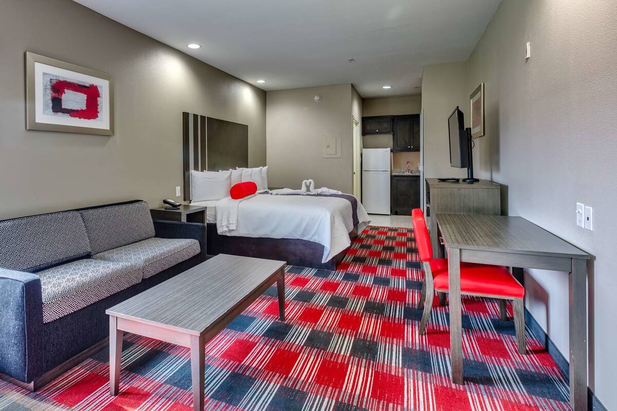 A hotel room with a bed, a sofa, a dining table, and a kitchen area.