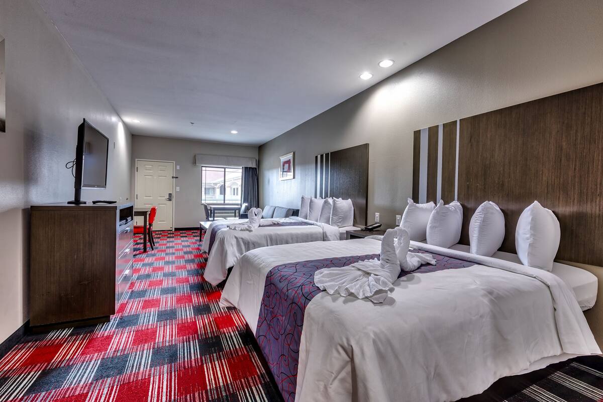 A hotel room with two beds, a desk, a TV, and a window with curtains.