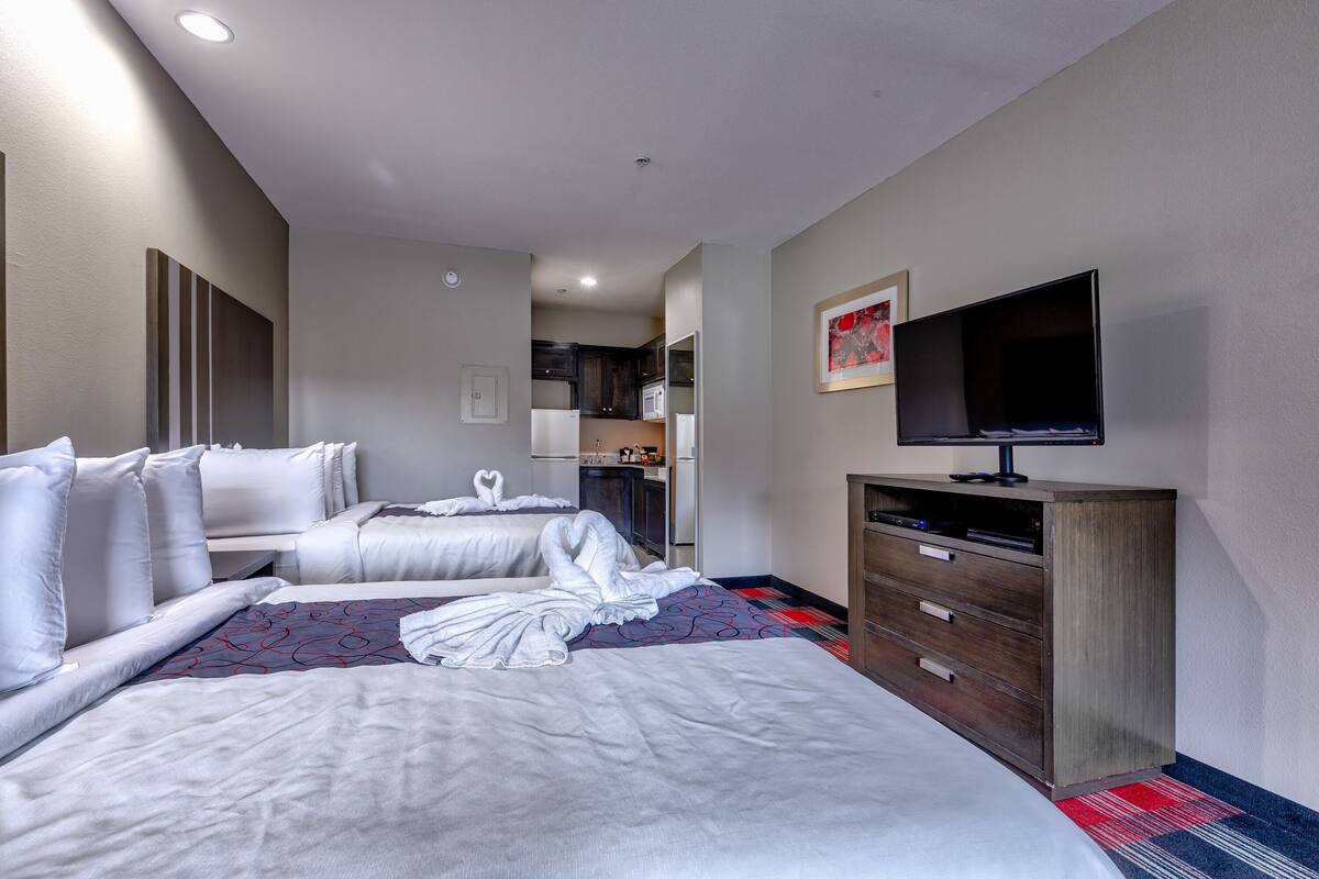 Une chambre d’hôtel avec deux lits, une télévision, une commode et, au fond, une petite cuisine.
