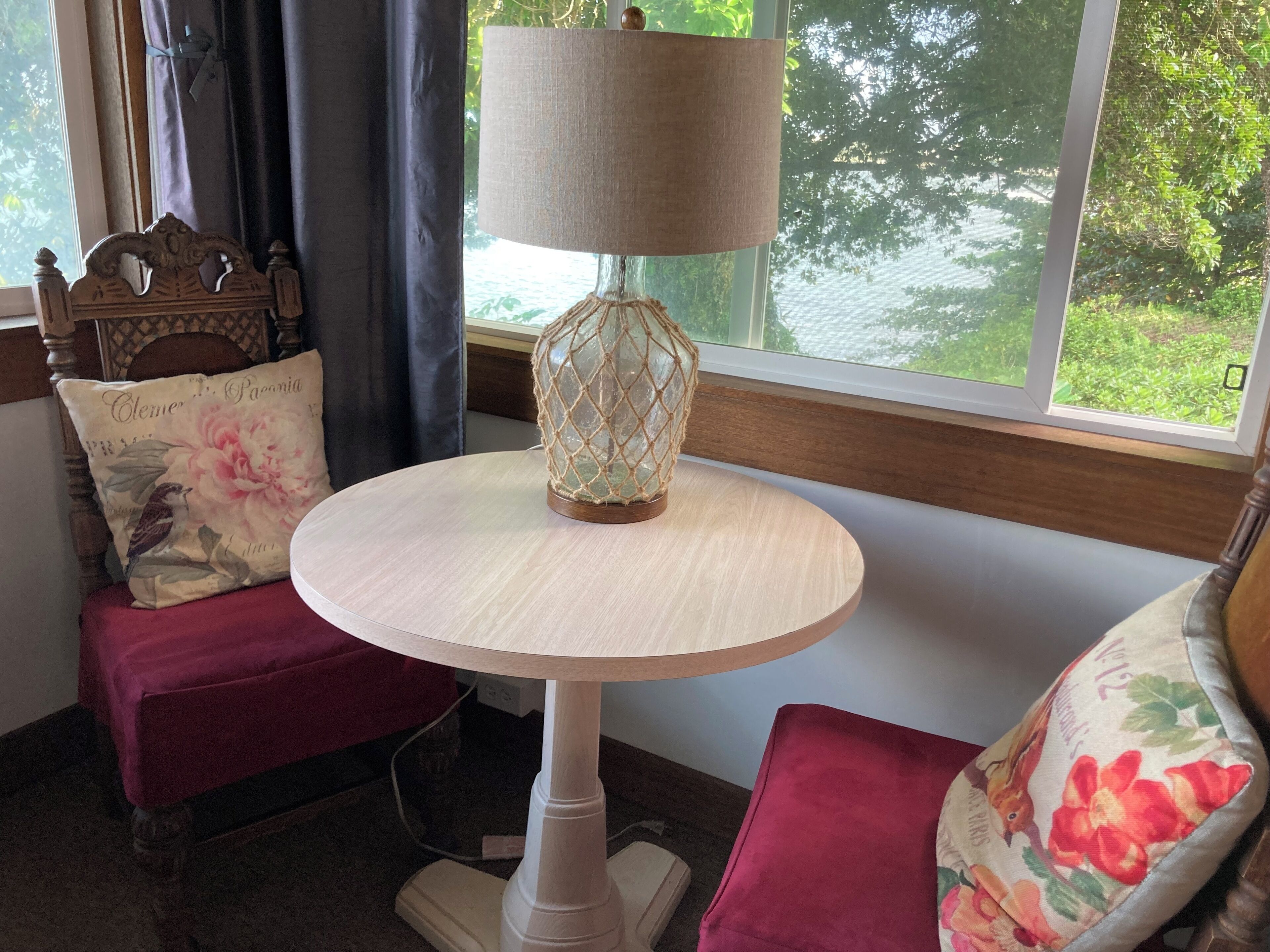 A round wooden table with a lamp and a cushion with a bird design.