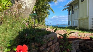 A house with a stone retaining wall, a palm tree, and a view of the ocean. - Hilo Bay Oceanfront B&B (Hilo)