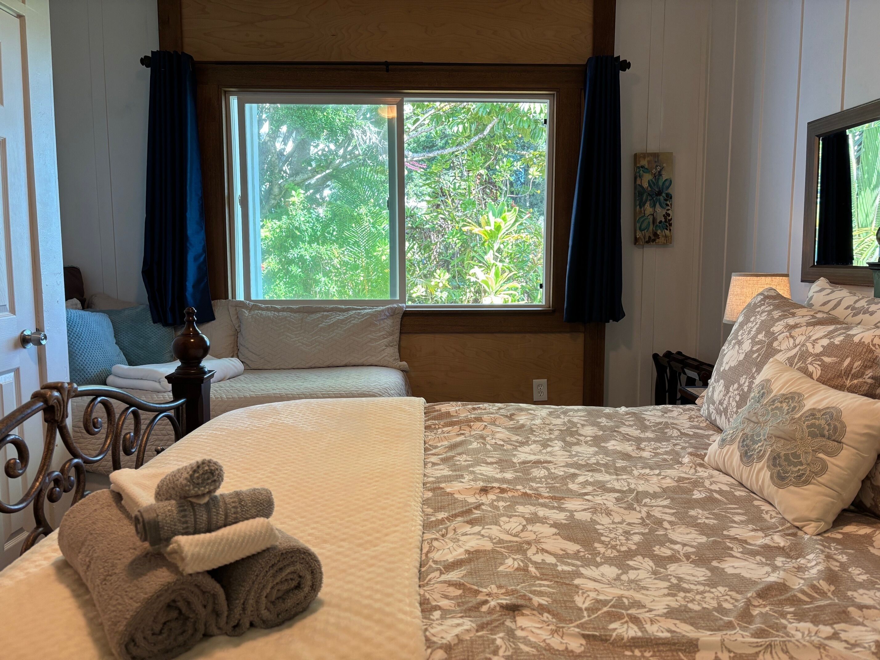 Une chambre avec un grand lit, une fenêtre avec des rideaux, une table de chevet et une lampe.