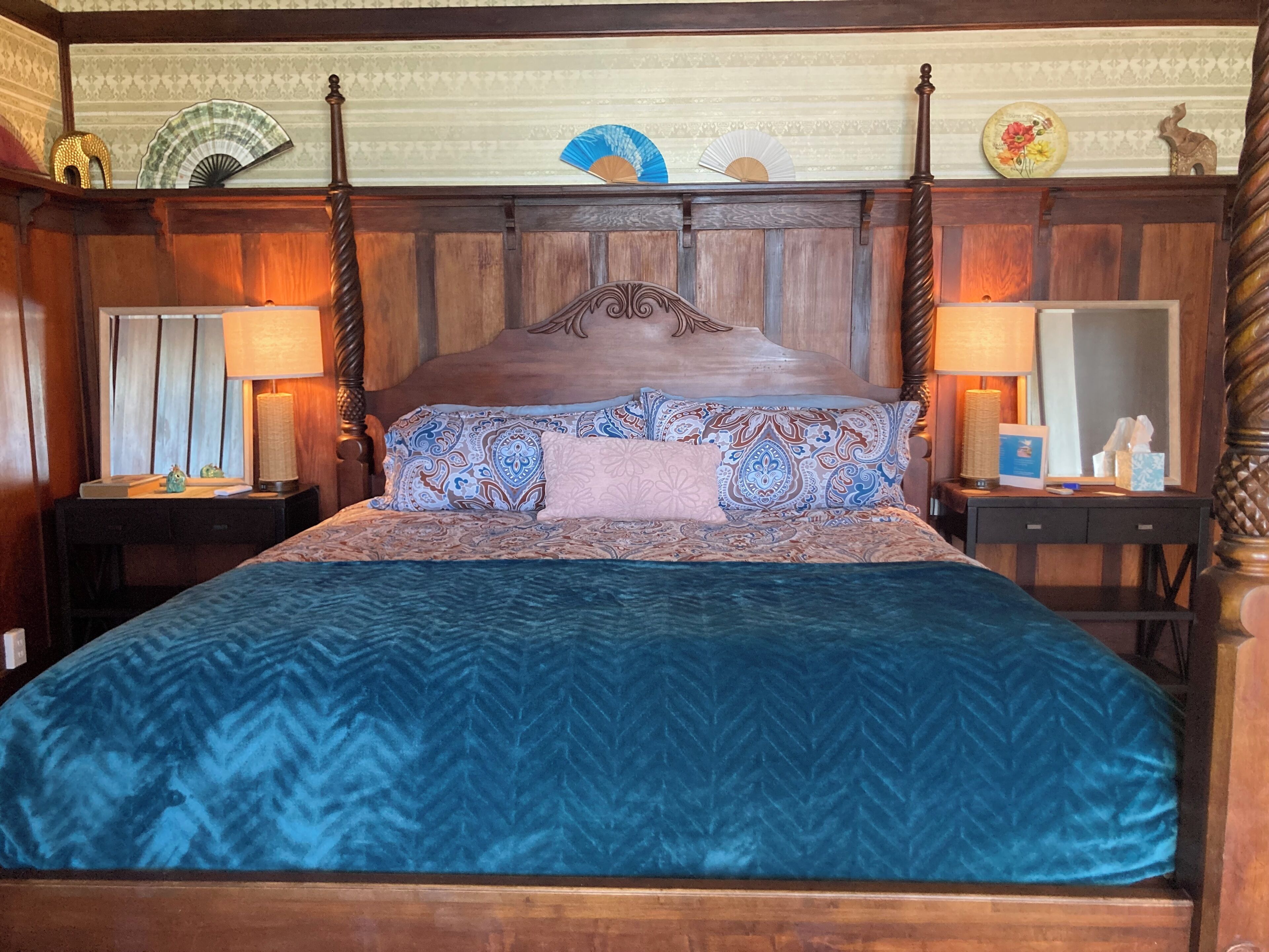 A bed with a herringbone-patterned duvet, a wooden headboard, and decorative fans on the wall.