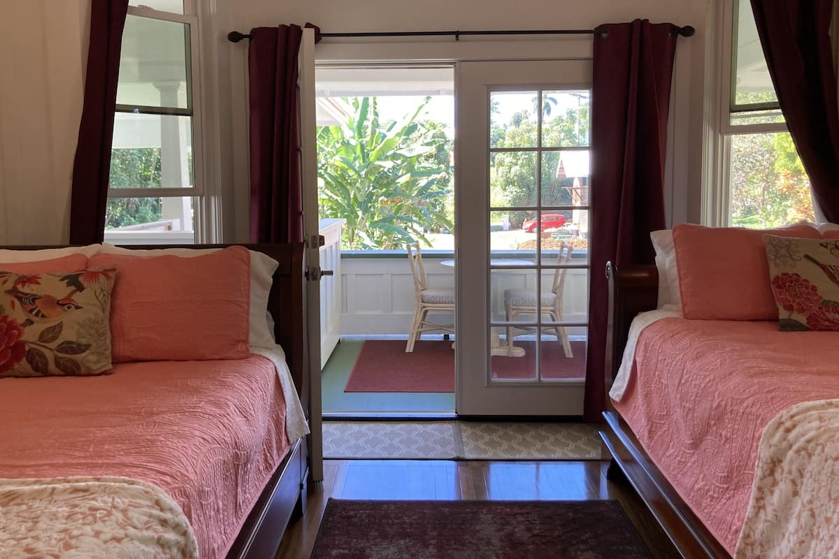 Habitación con dos camas, una puerta corrediza de vidrio que da a un espacio exterior con sillas y una mesa, y vistas al paisaje verde.