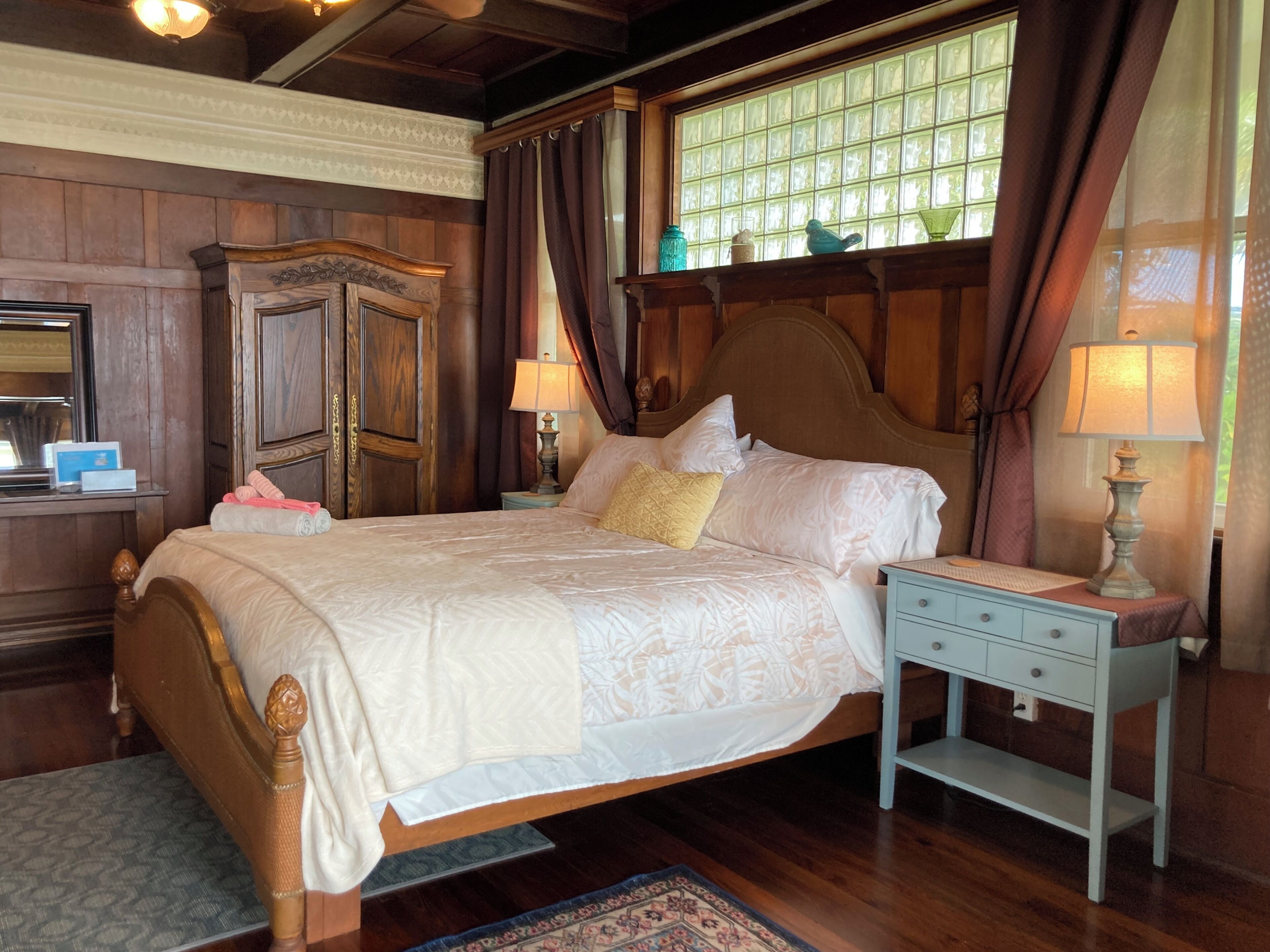 Een klassieke kamer met een groot bed, een houten hoofdbord en een nachtkastje met een lamp.