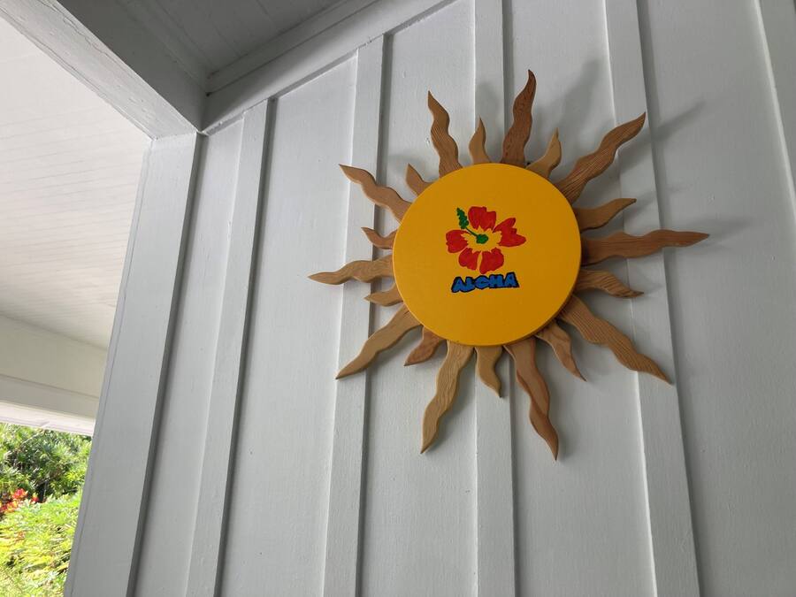 Decoração em formato de sol com uma flor e a palavra "Aloha" em uma parede branca.