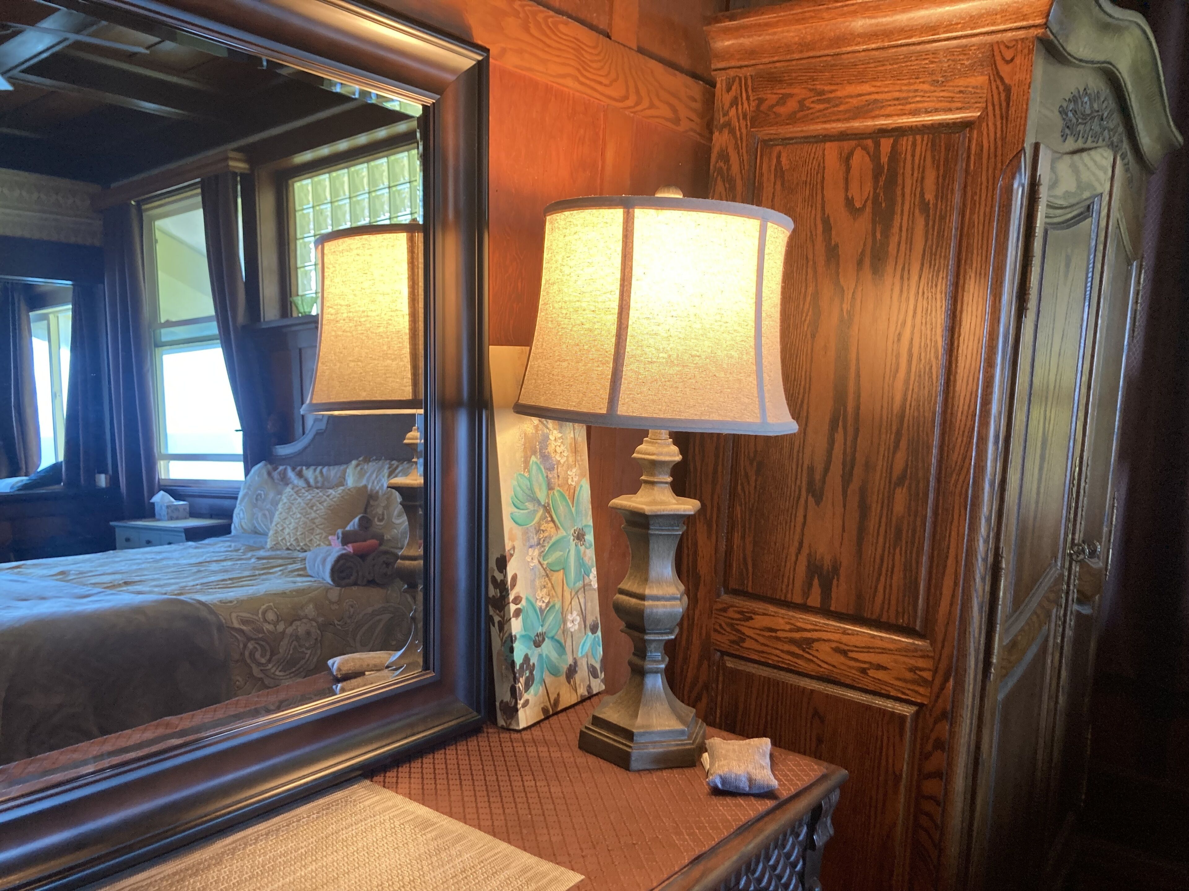 A wooden room with a large mirror, a lamp, and a bed with pillows.