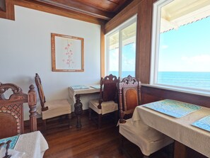 A room with wooden furniture, a table with a map, and a view of the sea through large windows. - Hilo Bay Oceanfront B&B (Hilo)