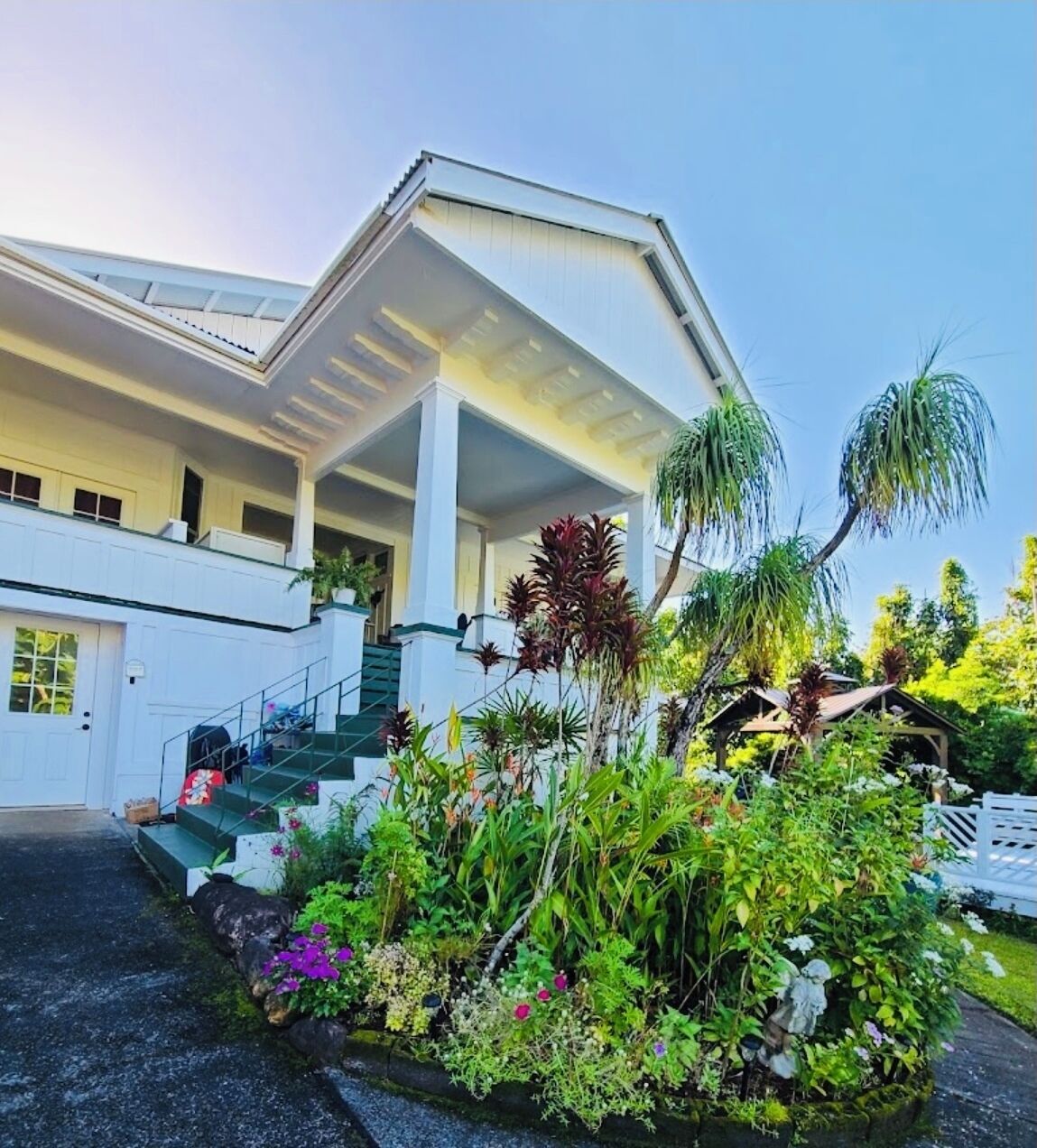 A two-story building with a covered porch, a staircase, and a garden with various plants.