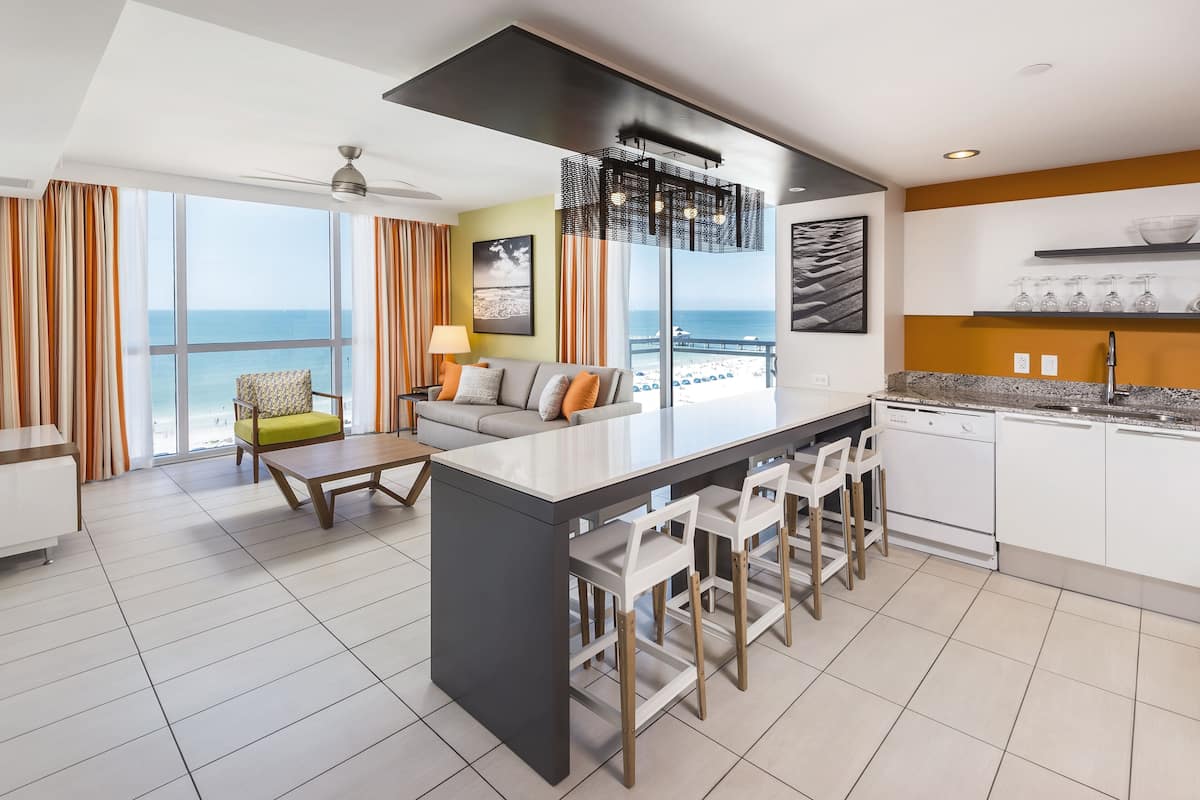 A modern kitchen with a central island, bar stools, and a view of the ocean.