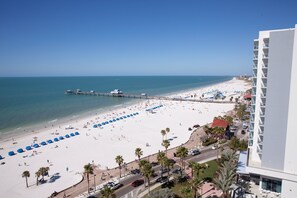 Una playa con un muelle, palmeras y un edificio blanco con balcones.