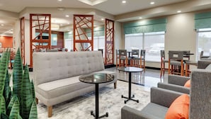 A modern hotel lobby with a sofa, tables, chairs, and decorative wooden partitions.