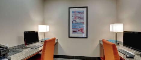 Habitación de hotel con dos escritorios, cada uno con una computadora, teclado y ratón. Hay dos lámparas en cada escritorio y un cuadro abstracto enmarcado en la pared.