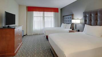 Habitación de hotel con dos camas, televisor, escritorio y ventana con cortinas.