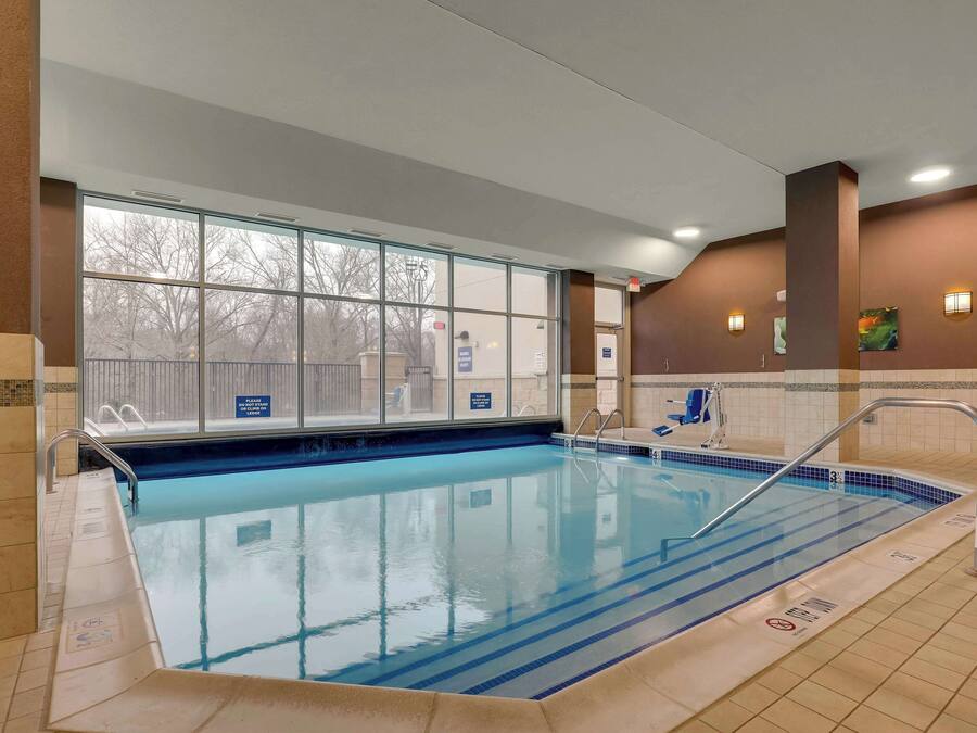 An indoor swimming pool with clear glass walls, a tiled floor, and a metal ladder.