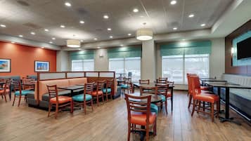 Un restaurante con cabinas y mesas, piso de madera y ventanas amplias.
