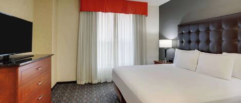 A hotel room with a large bed, a wooden dresser, a flat-screen TV, and a window with curtains.