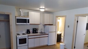 A compact kitchen with white cabinets, a microwave, a stove, a refrigerator, and a sink. - Florence Motel (Smithers)