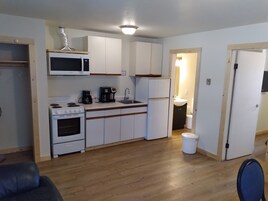 Una cocina compacta con gabinetes blancos, un microondas, una estufa, un refrigerador y un lavabo.