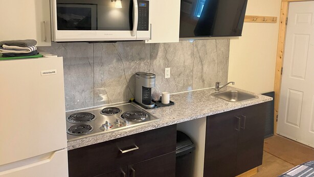 A compact kitchen with a microwave, stove, and coffee maker. - Florence Motel (Smithers)