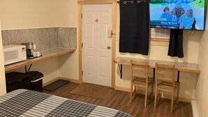 A small hotel room with a bed, a desk with a microwave, a TV, and a chair. - Florence Motel (Smithers)
