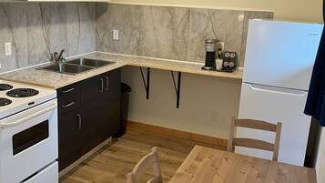 A compact kitchen with a built-in oven, microwave, and refrigerator. There's a wooden dining table and a single chair.
