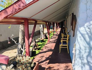 A covered outdoor area with a wooden deck, chairs, and a cactus garden. - Historic Shep's Miners Inn near Kingman (Chloride)