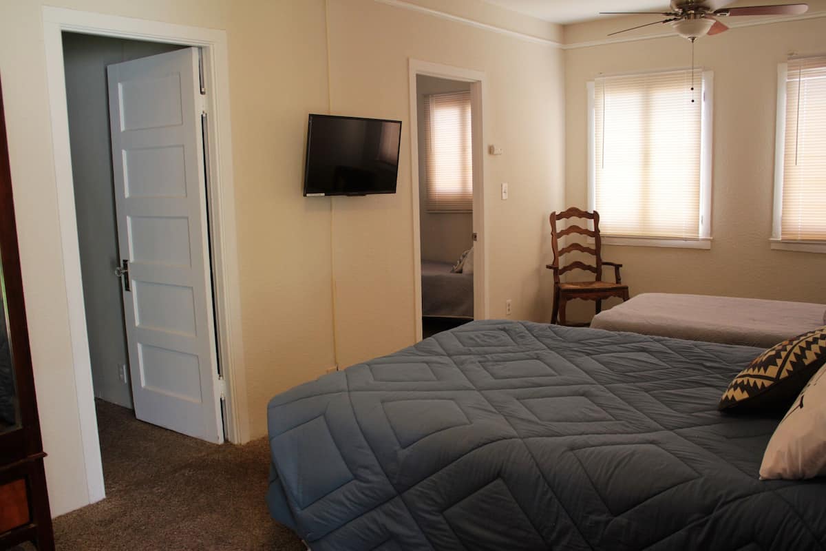 A bedroom with a bed, a television, a ceiling fan, and a chair.