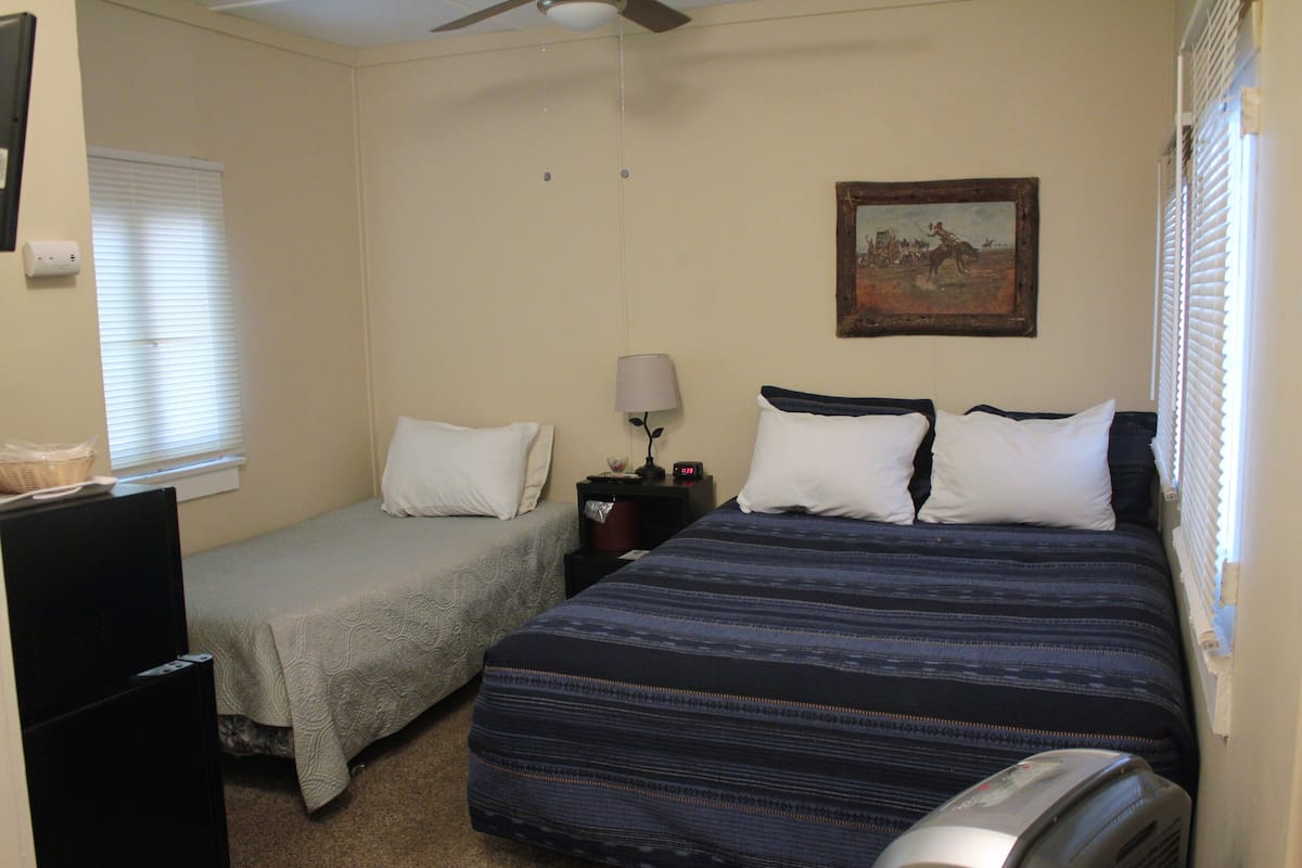 A bedroom with two beds, a ceiling fan, a painting on the wall, and a window with blinds.