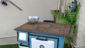 A blue vintage stove with a metal bowl on top, placed on a grassy area.