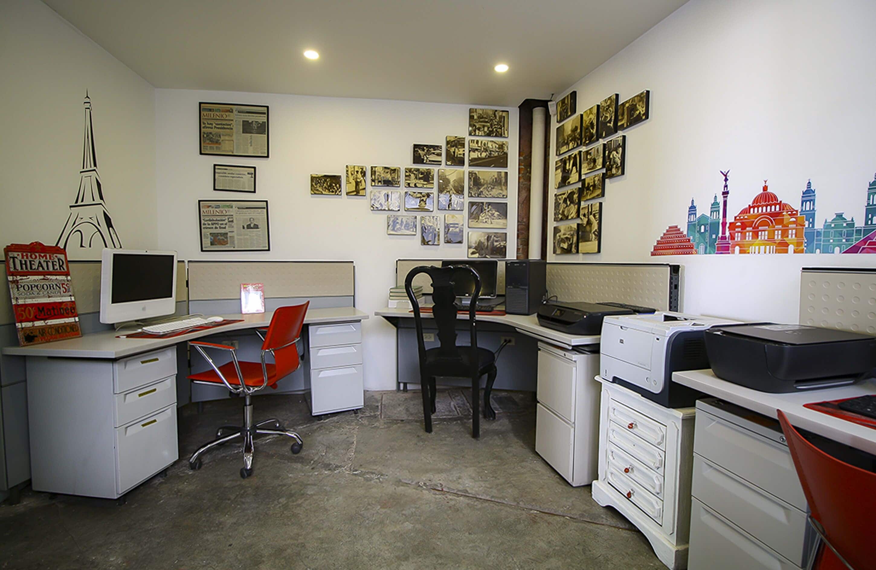 A small office with a desk, chair, and filing cabinets. There are framed pictures on the wall and a computer monitor on the desk.