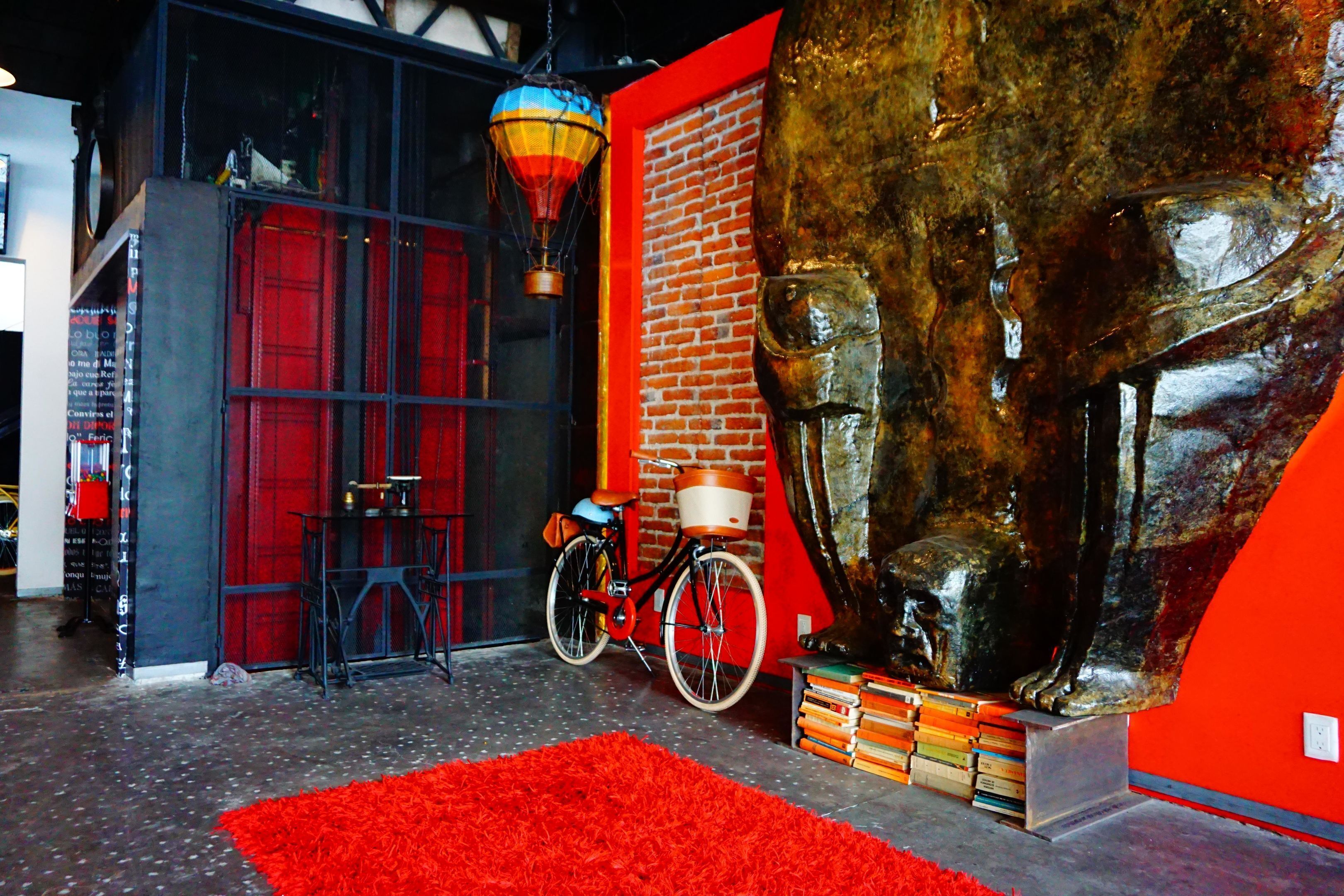 Una habitación con alfombra roja, una escultura de bronce grande, una bicicleta y una pared de ladrillo.