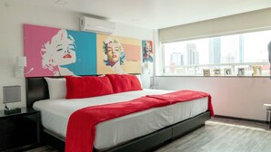 Una habitación de hotel moderna con una cama grande, ropa de cama roja y llamativos cuadros de arte pop en las paredes.