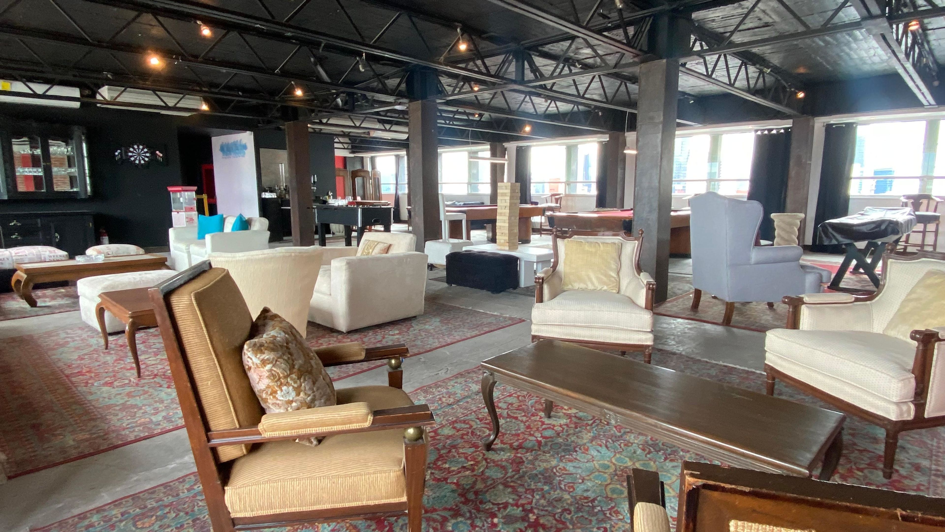 Un salón amplio con diversas opciones de asientos, incluyendo sofás y sillones, una mesa de billar y un dardo.