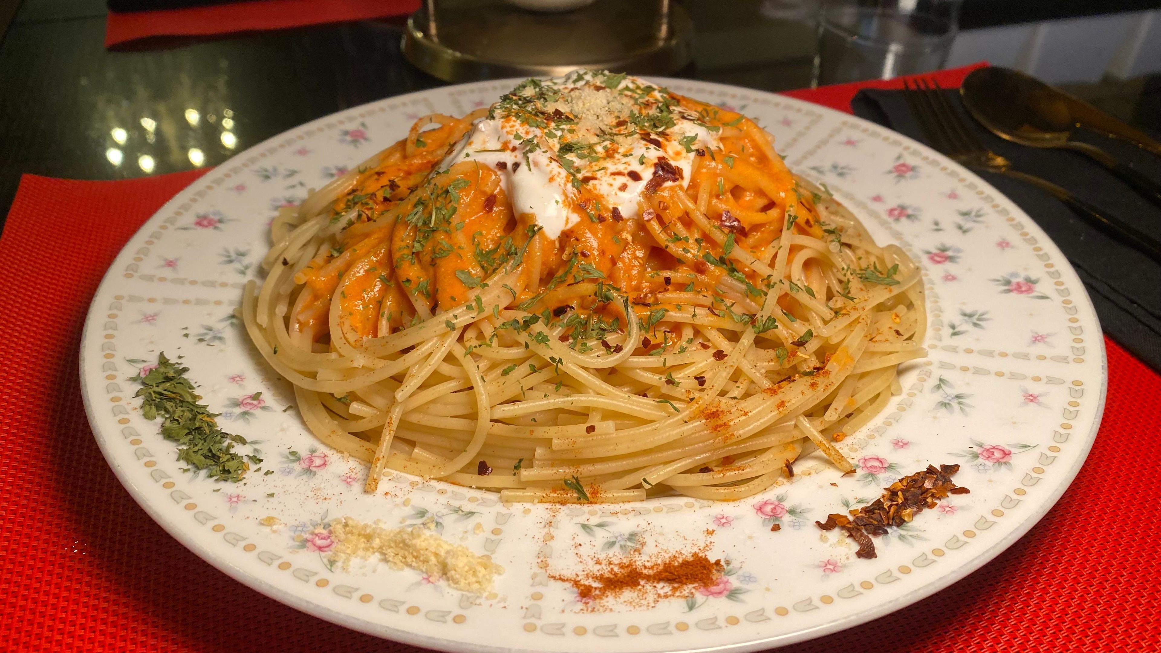 A plate of spaghetti with a creamy sauce, garnished with herbs and spices, on a floral-patterned plate.