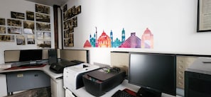 Una oficina moderna con escritorio, computadora, impresora y una pared con un mural de un paisaje urbano colorido.