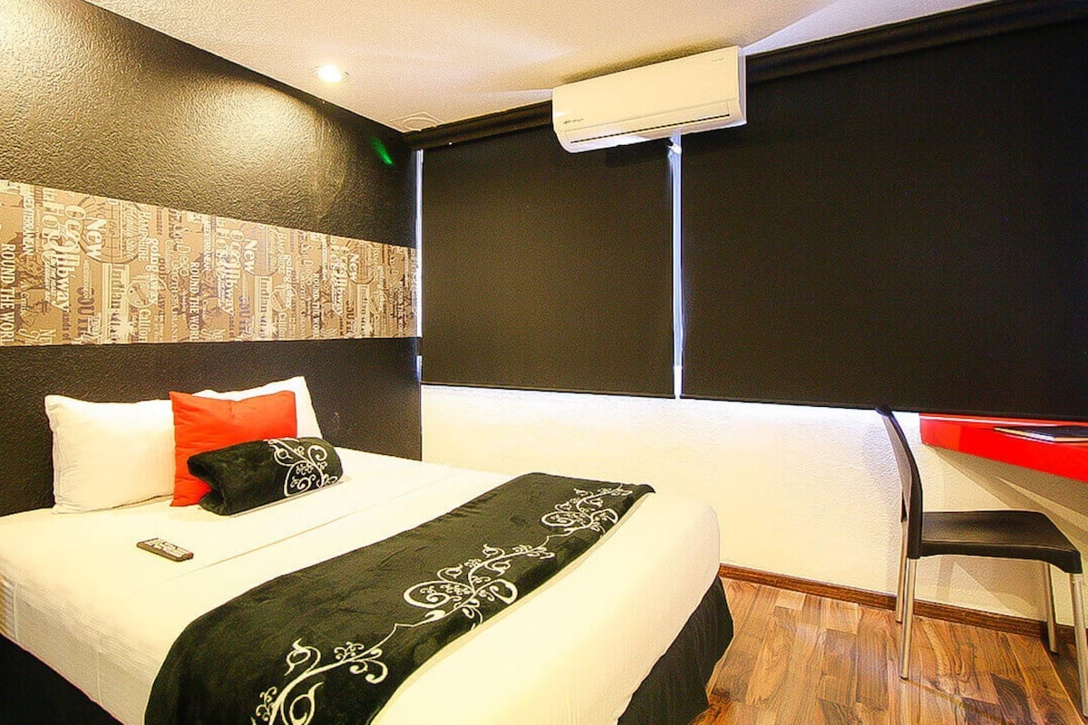 Una habitación de hotel con una cama, un escritorio y un equipo de aire acondicionado.