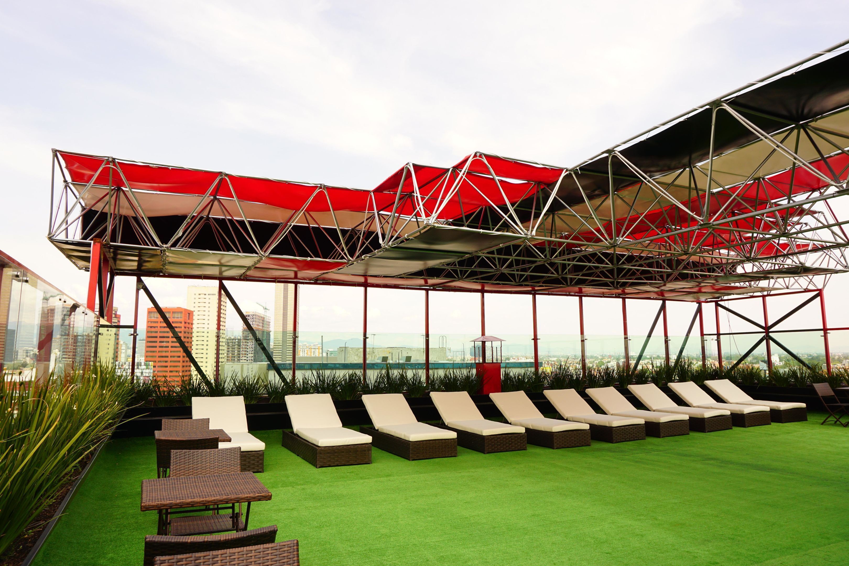 Un área de lounge en la azotea con un toldo rojo, césped artificial verde y varias sillas de lounge.