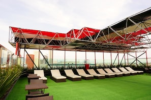 A rooftop lounge area with a red canopy, green artificial turf, and multiple lounge chairs. - Hotel Black (Mexico City)