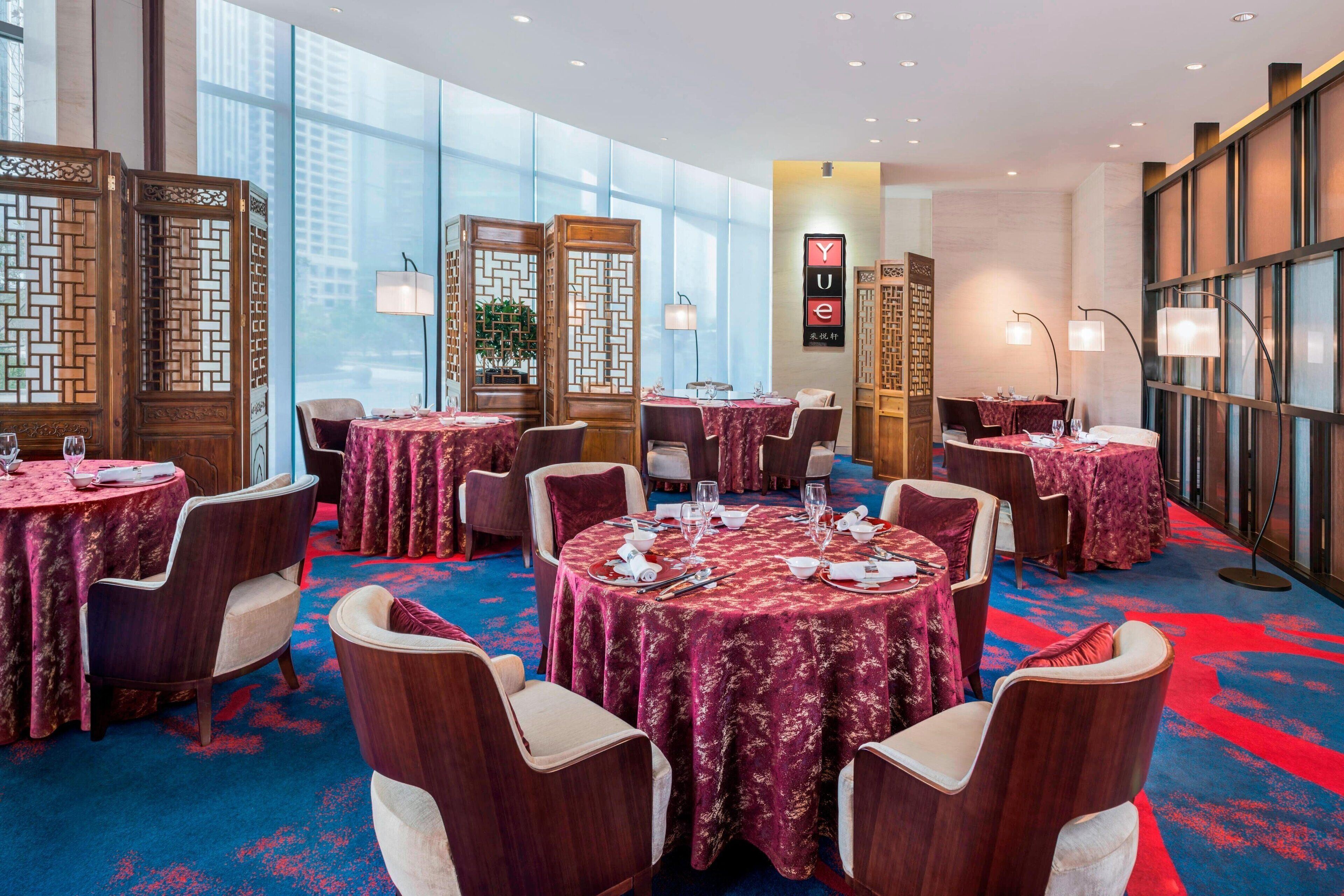 Een restaurantgedeelte in een hotel met ronde tafels, stoelen en een blauw tapijt.